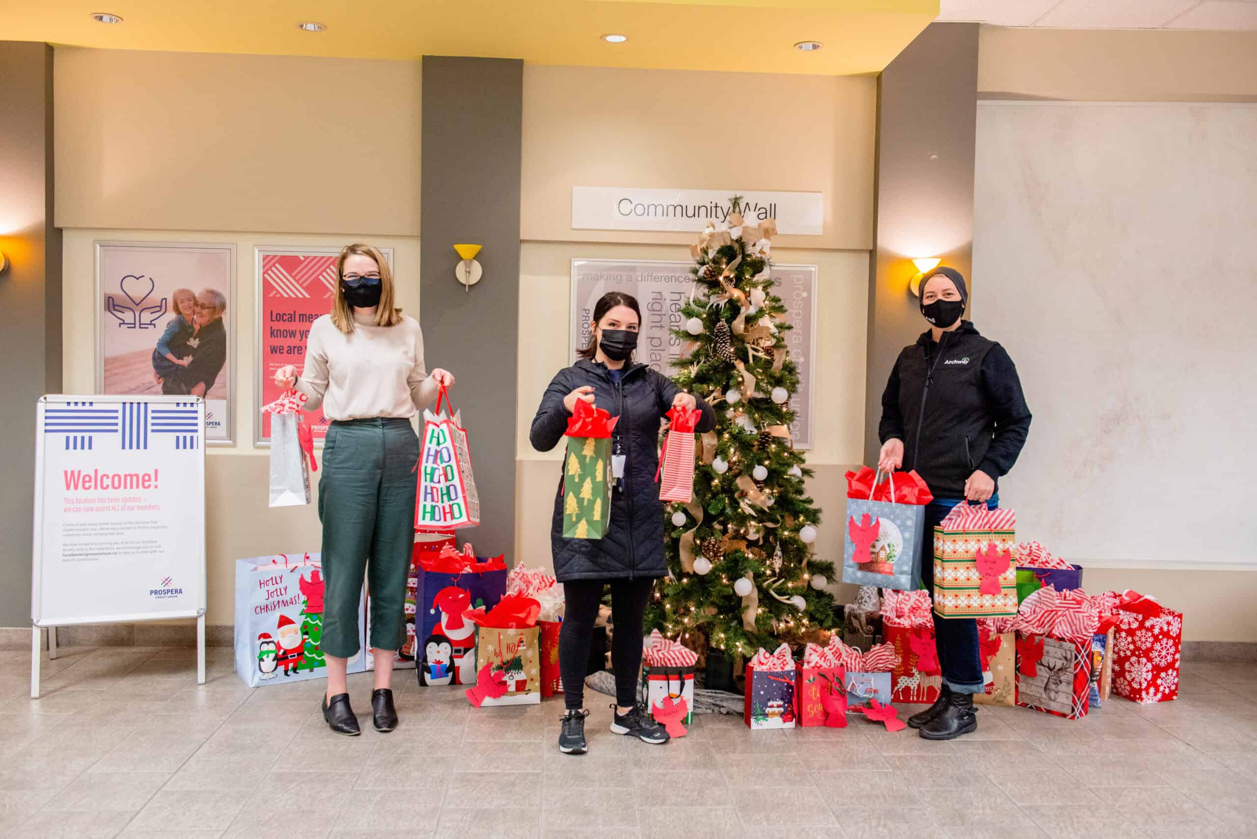 Angel Tree Three women infront of a Christmas tree holding gifts