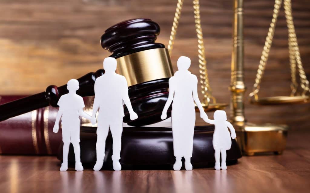 family figure cut out in front of a judge's gavel and the scales of justice on a desk