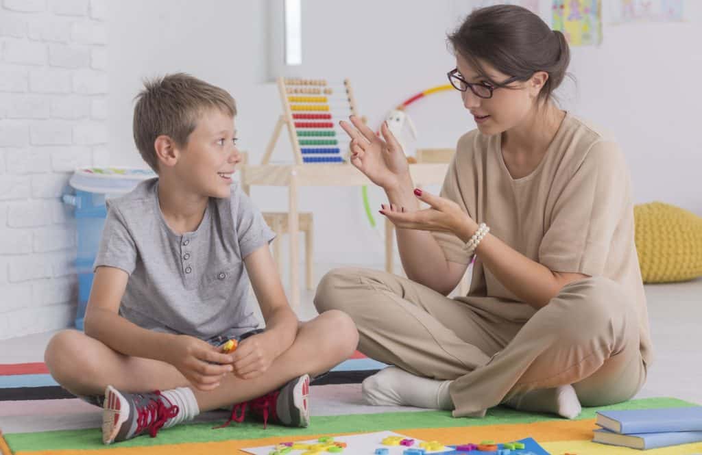 therapist teaches young boy while sitting on floor together