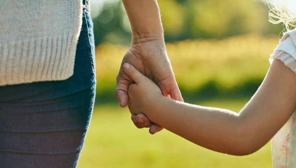 little girl holding parent's hand outside, representing peaceful and supportive parenting