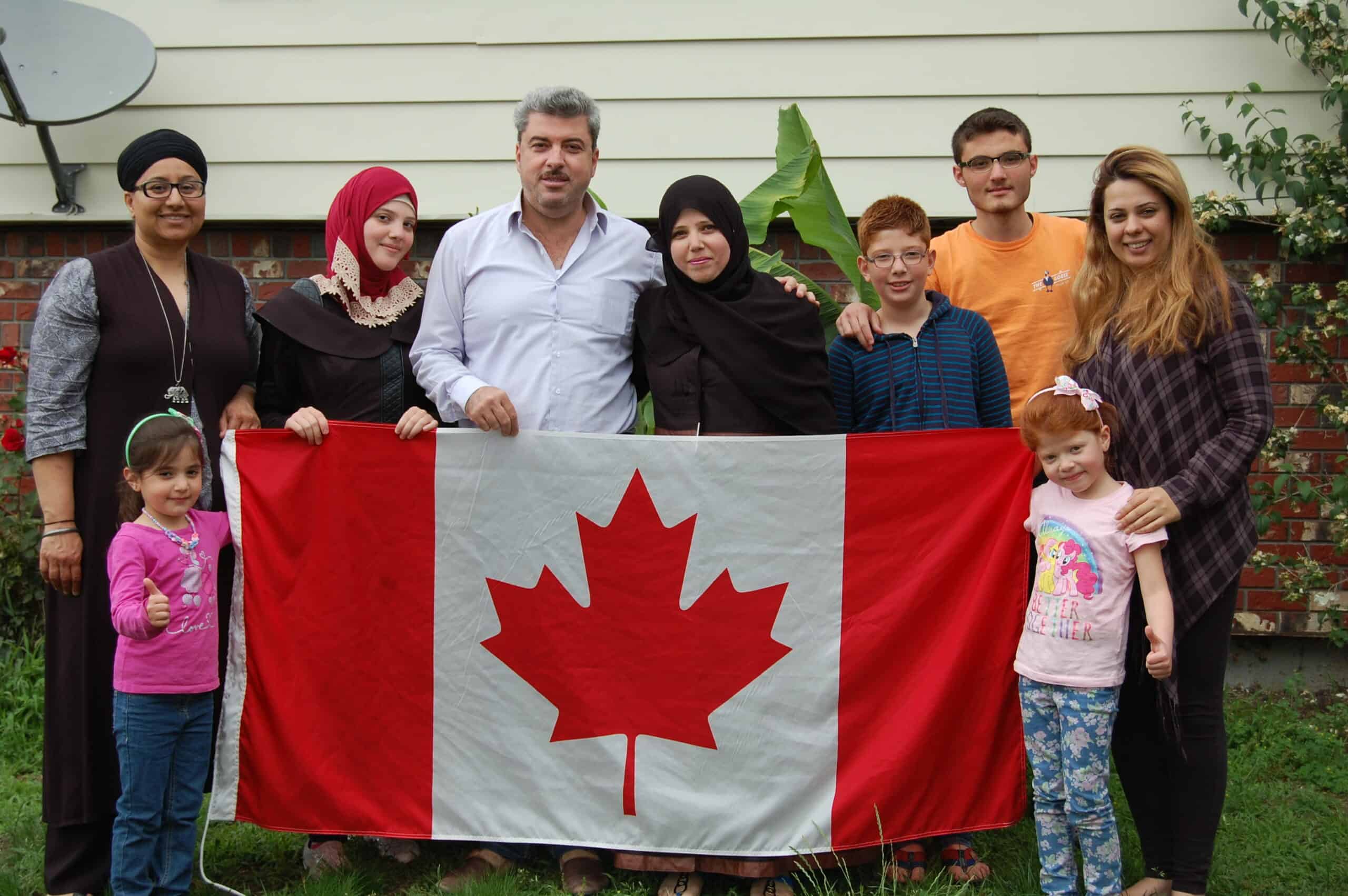 Syrian Refugee families stand together holding a Canadian flag.