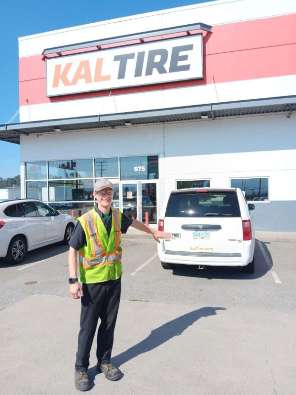 Young adult male poses in front of tire company building and mini van
