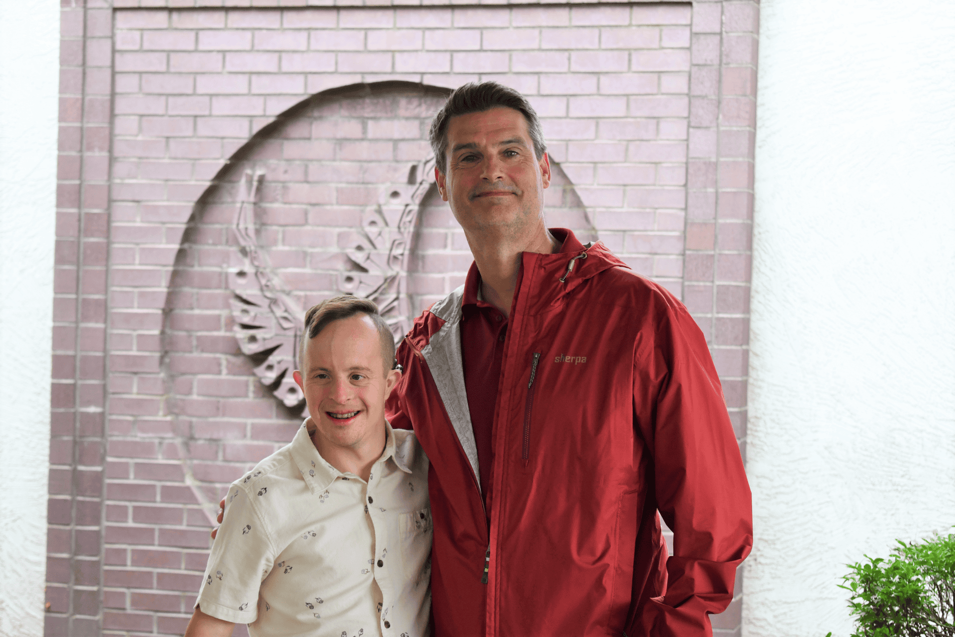 Young adult male with Down syndrome poses with adult male in front of building