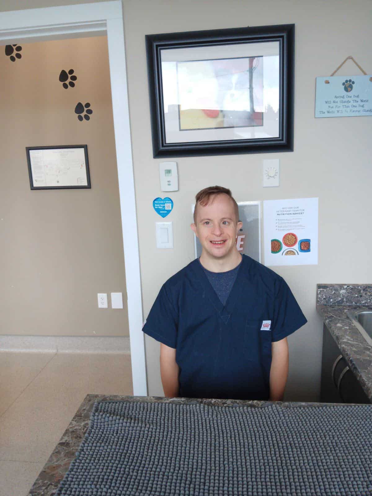 Young adult male with Down Syndrome sits behind counter at animal hospital smiling