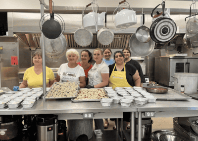 Group of volunteer cooks in industrial kitchen with trays of food on table