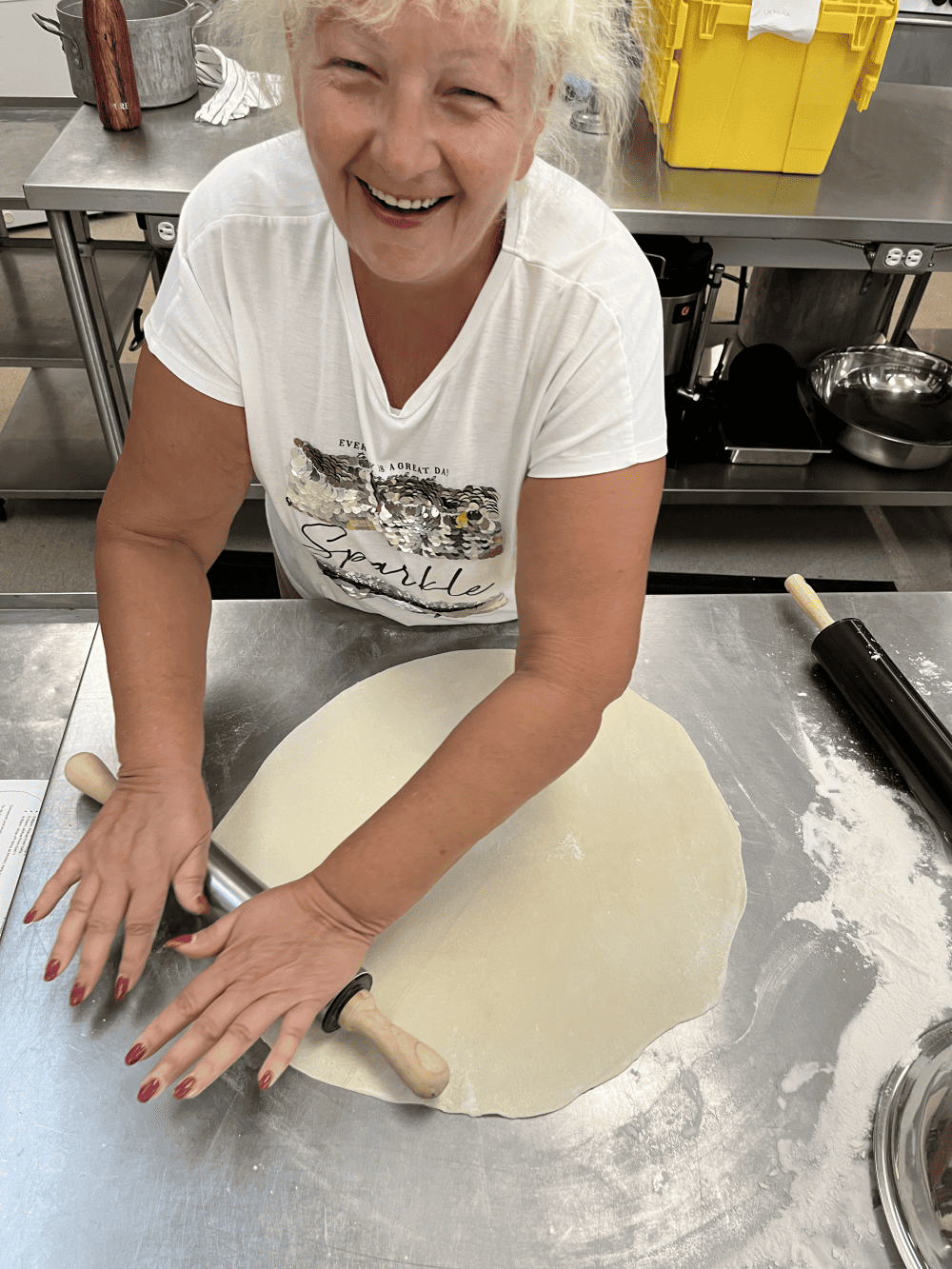 Smiling older adult female rolls out flour dough with rolling pin