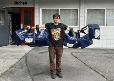 Young adult holds seven insulated food delivery bags on arms with arms stretched out