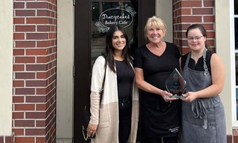 three women smile at camera in front of brick store front.