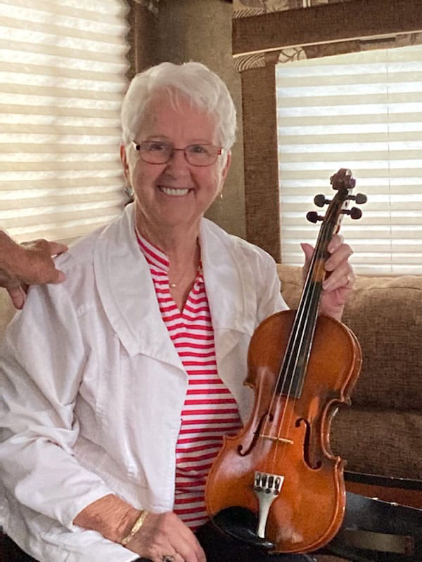 Senior woman smiles at camera while holding a violin