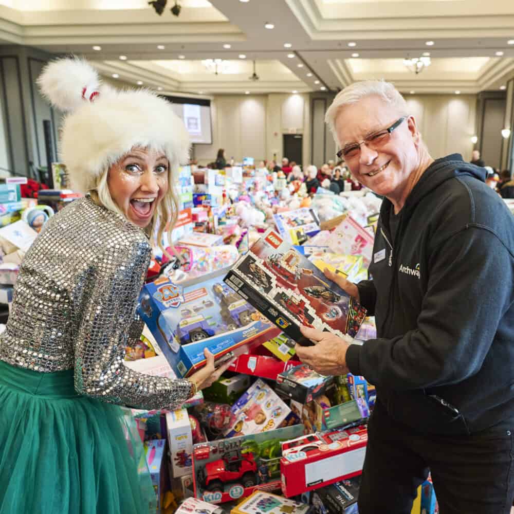 Man and woman pose in front of pile of toys and smile at camera