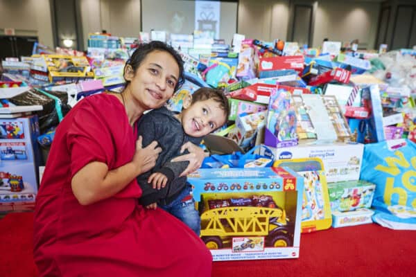 A mother and child pose in front of a pile of toys