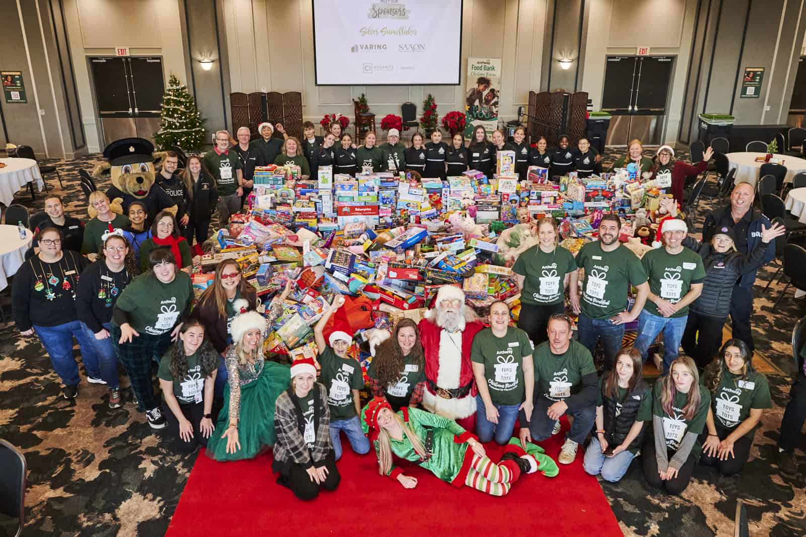 Group of people pose around a large pile of toys