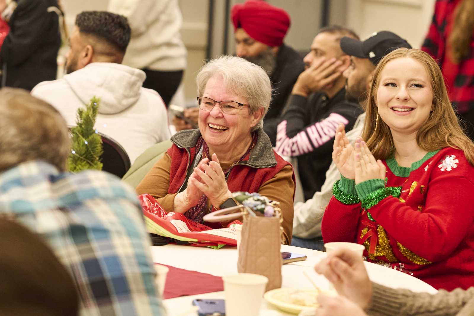 older woman sits at dining table clapping and smiling at event