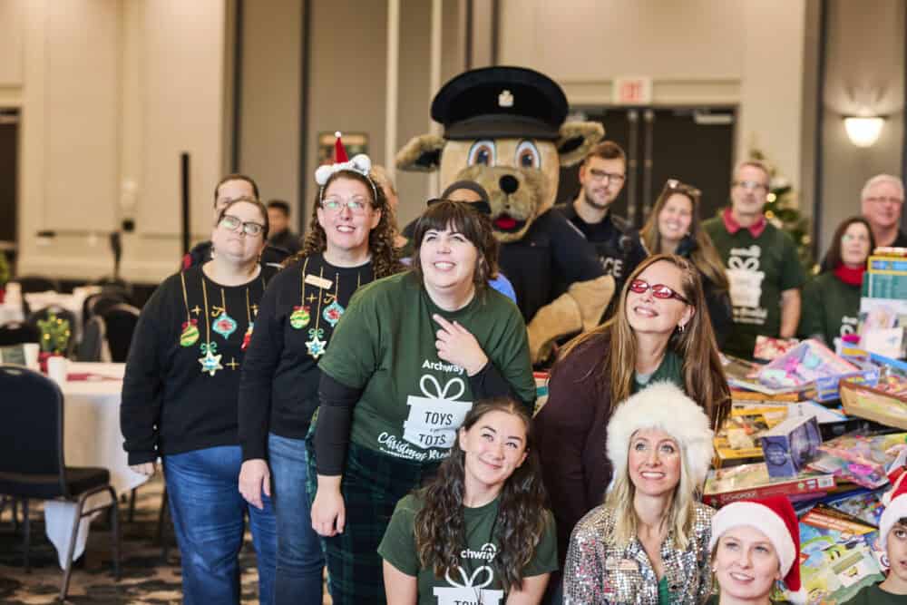 Group of people pose with canine police mascot with large piles of toys behind them
