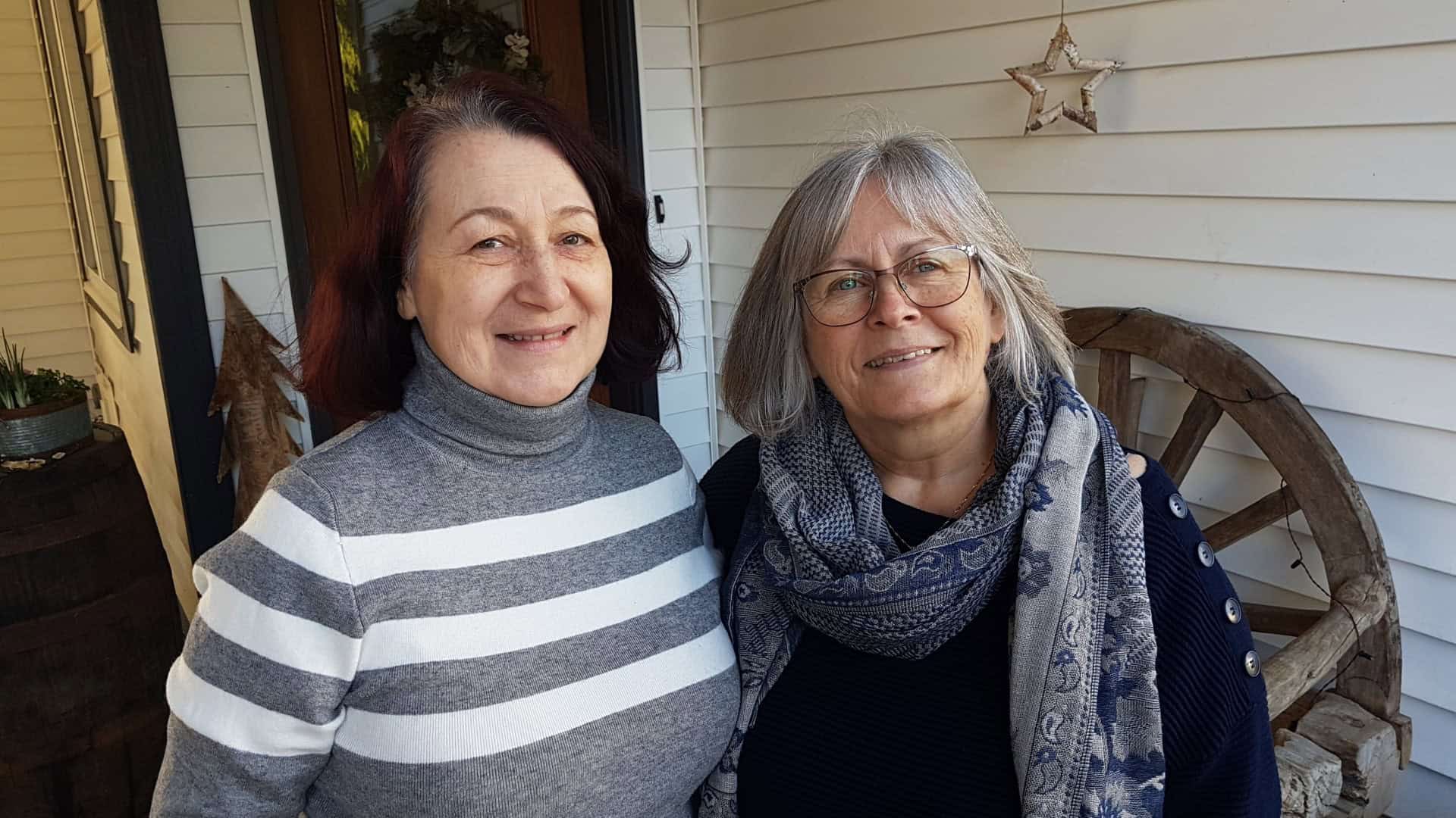 Two women stand on front porch smiling at camera