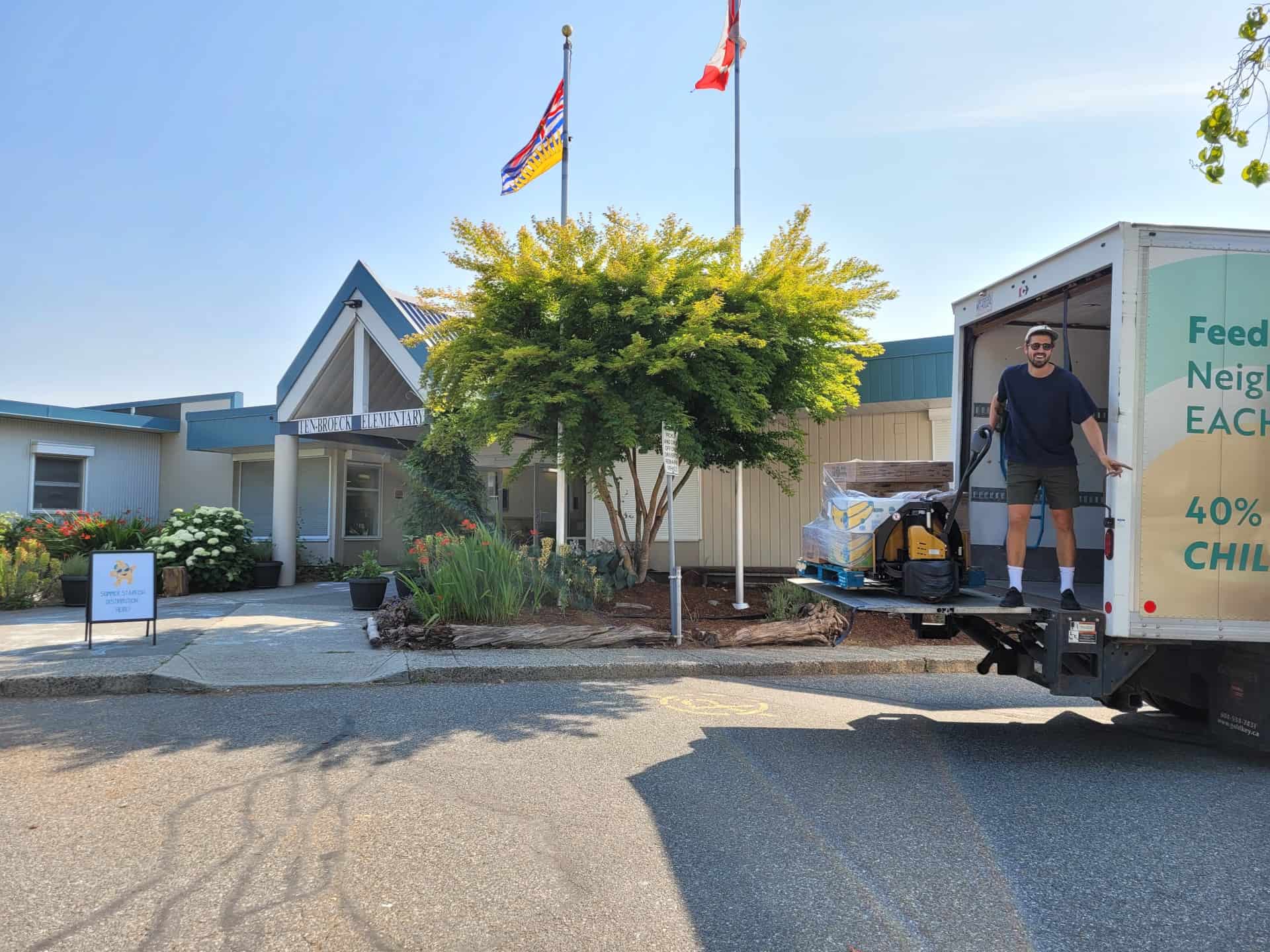 Man stands on the back of a loading truck in front of an elementary school