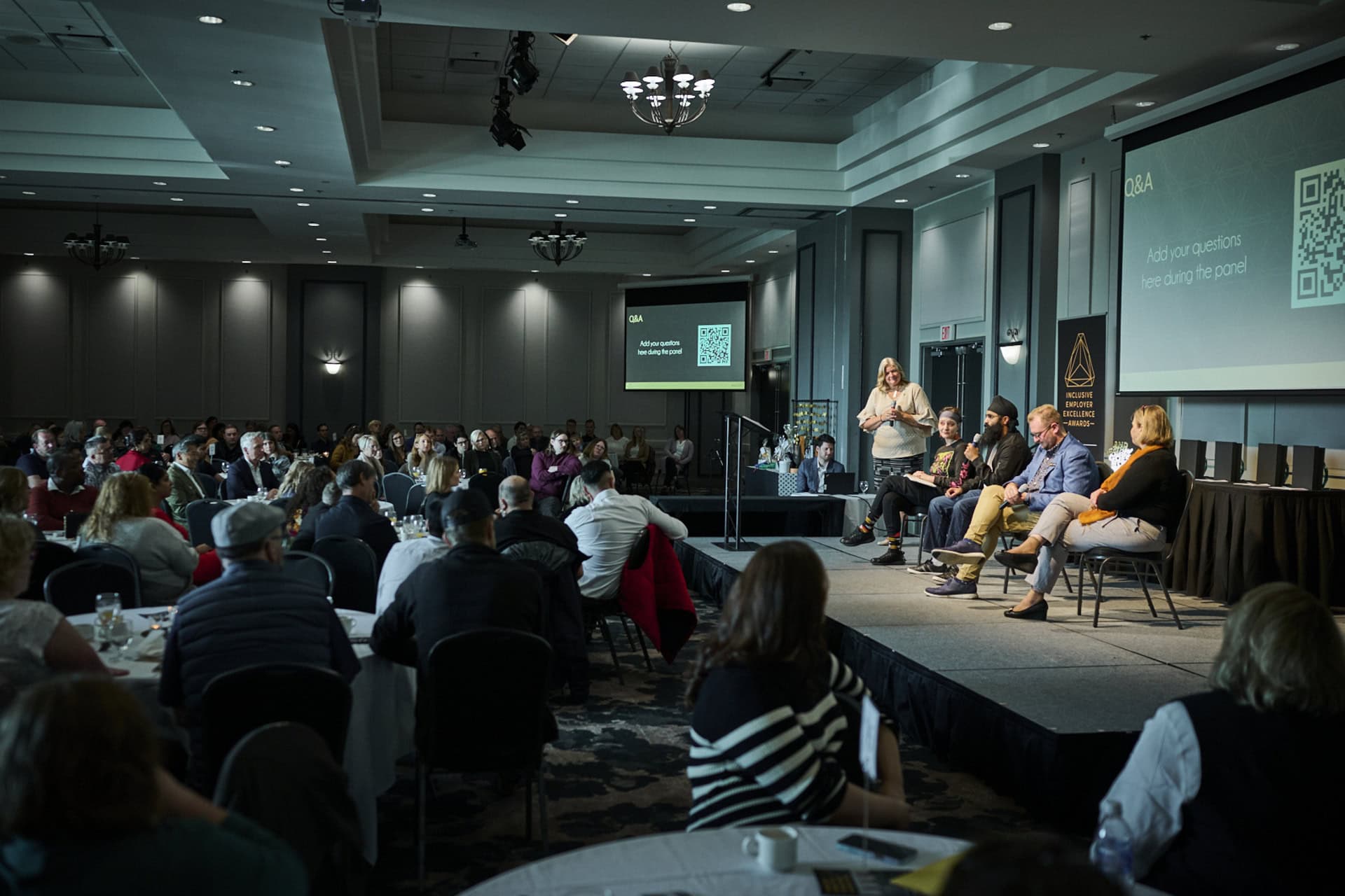 Group of people on stage smiling at the camera with the inclusive employer excellence logo behind them on a projector screen