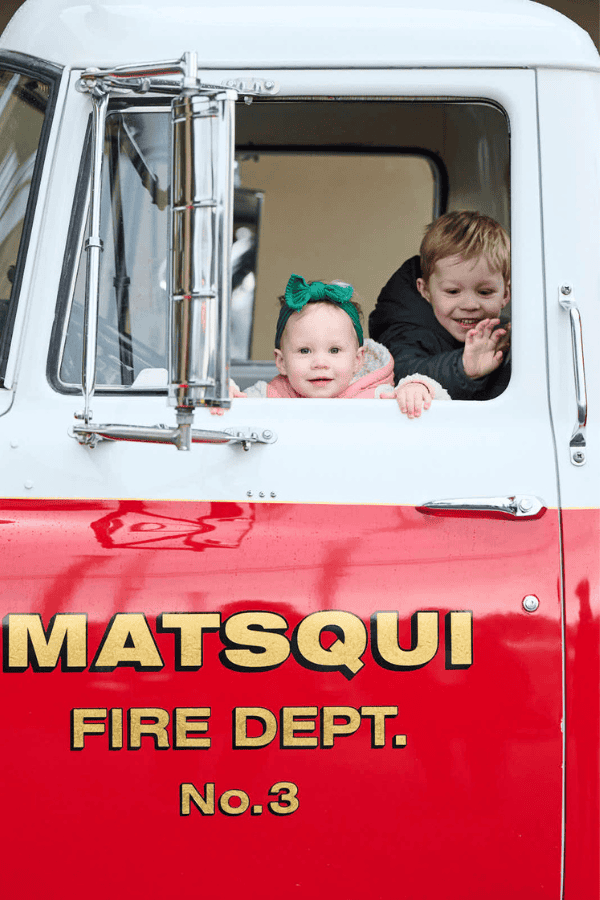 2 young toddlers sit in a fire truck driver seat