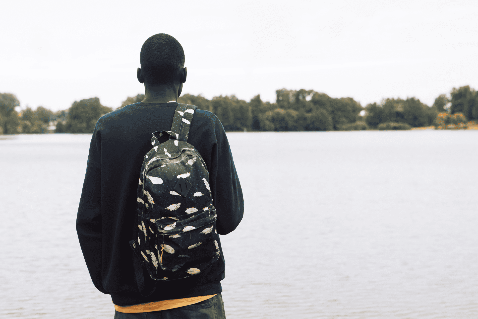 Man wearing a backpack looks at lake with back turned to camera.