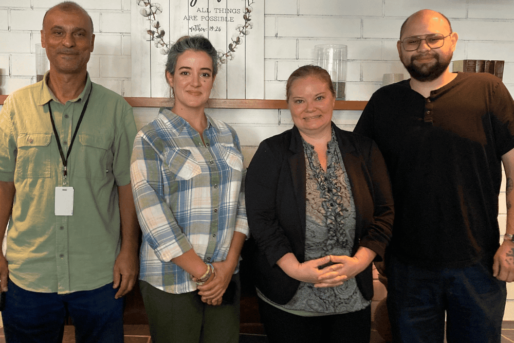 Group of four people stand abreast smiling at camera.