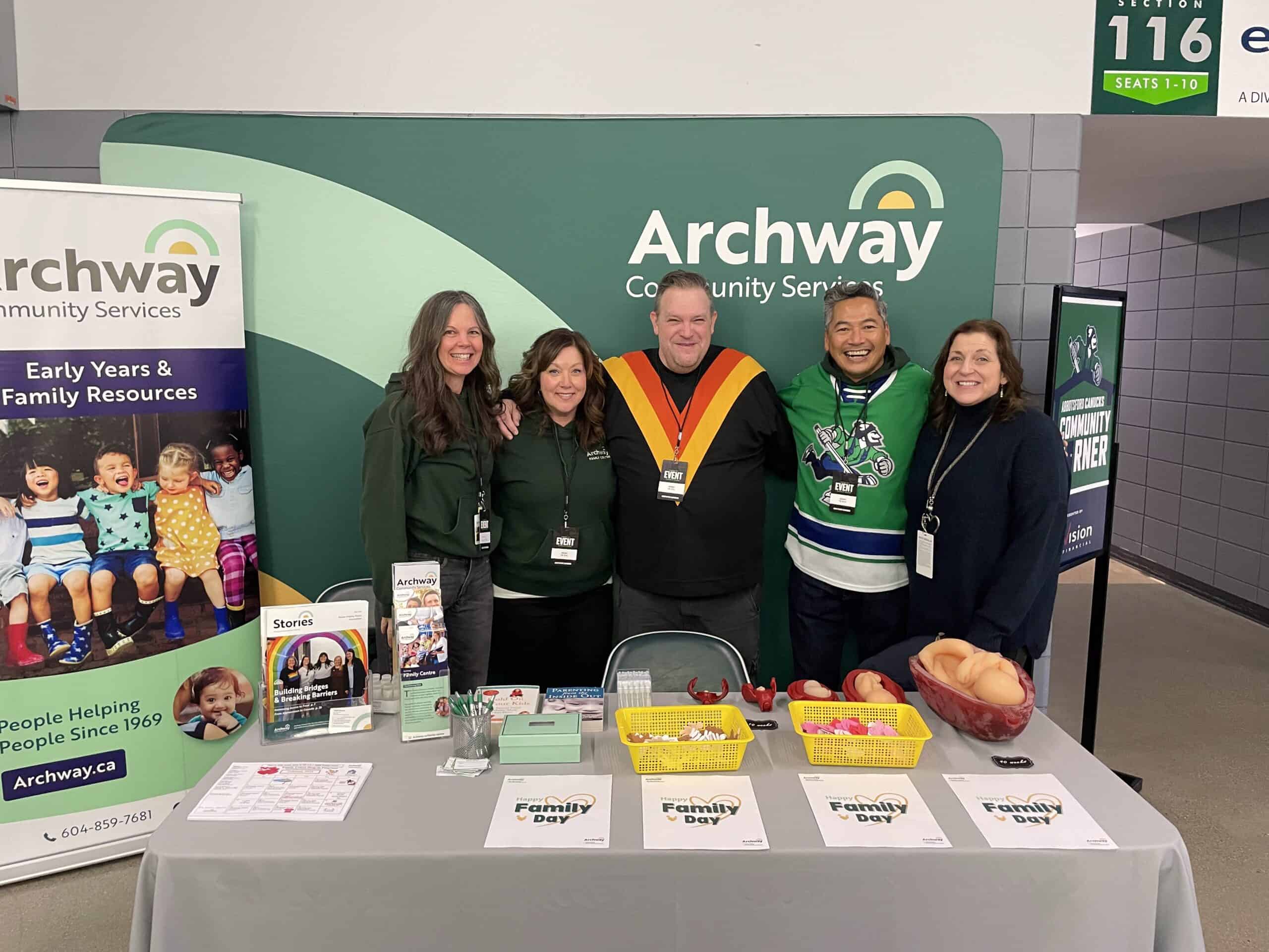 Archway staff stand in front of Archway banner at table for Family Day.