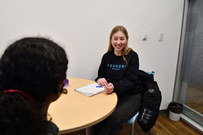 A teenager smiling, sitting across the table from another young individual 