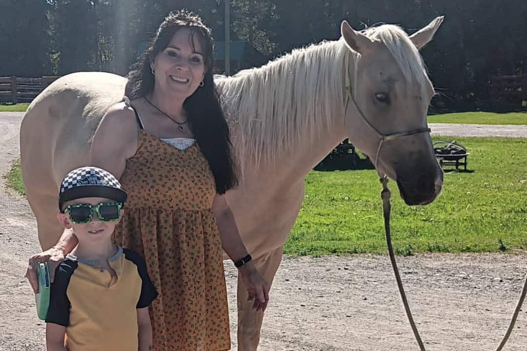 A woman and a young boy stand next to a horse smiling at the camera