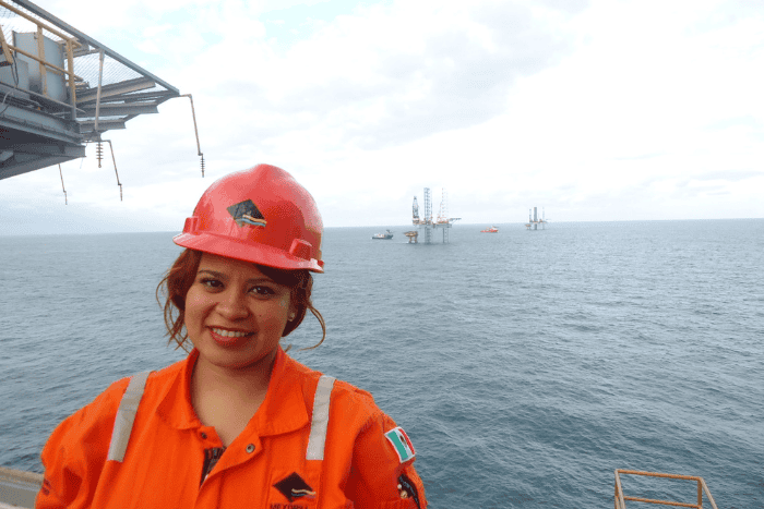 Woman in hardhat in foreground with jack up oil rigs in background on the ocean