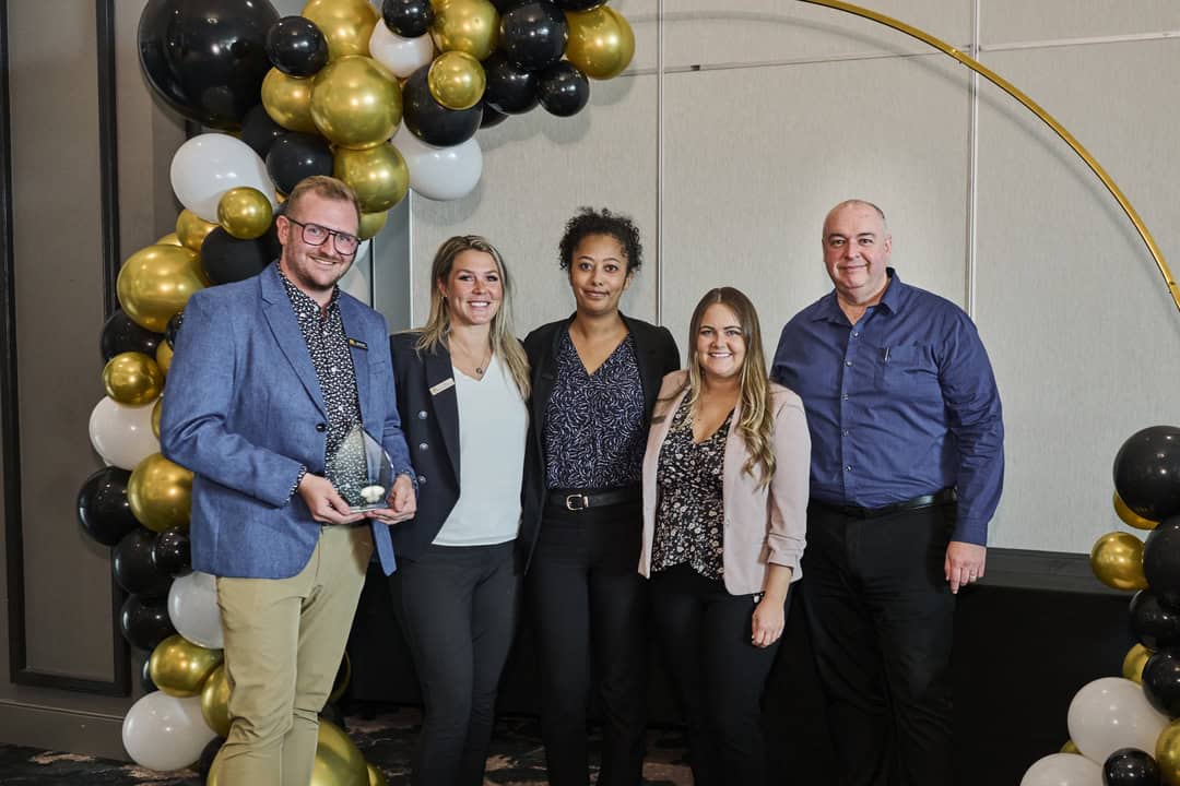 Group of five people posing for a picture holding an award.