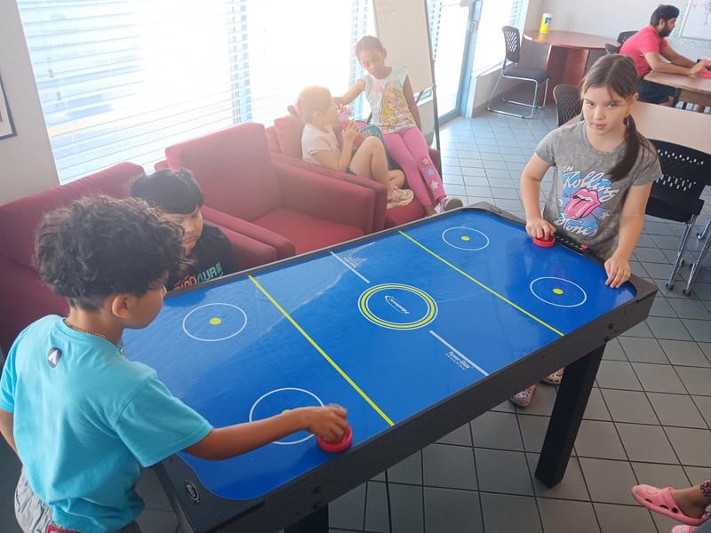 Kids playing air hockey in a room with a table.