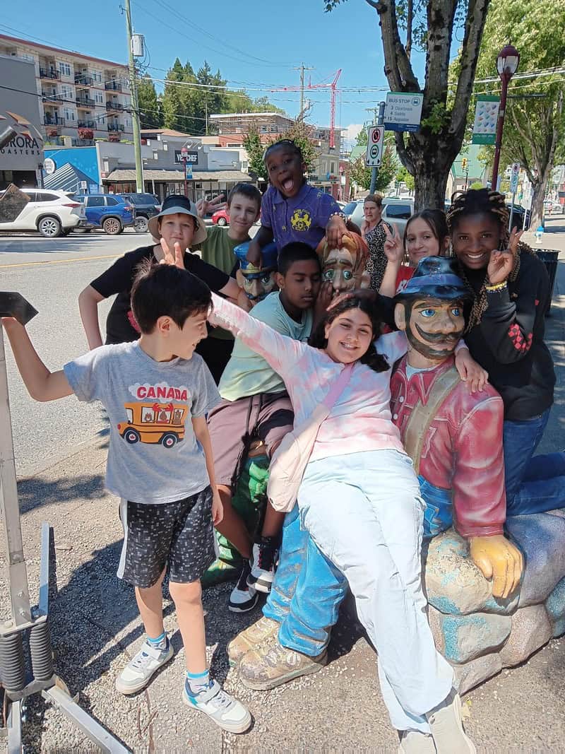 A group of kids posing with a statue of a man.