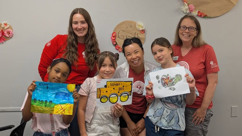 A group of children holding up their artwork in front of three adults.