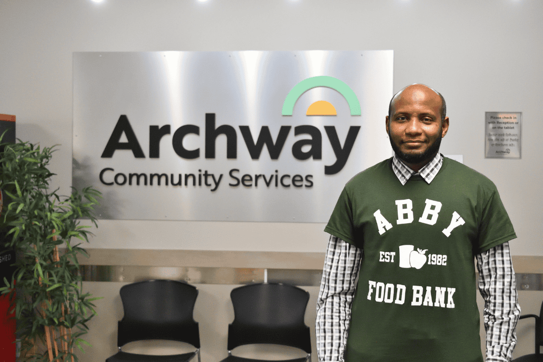 Din standing indoors in front of Archway sign