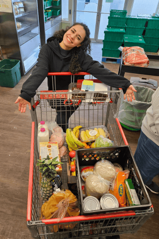 Hiva smiling, posing with arms sprawled across both sides of buggie full of food