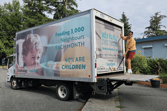 Colin standing on back of Food Bank truck, giving a thumbs up