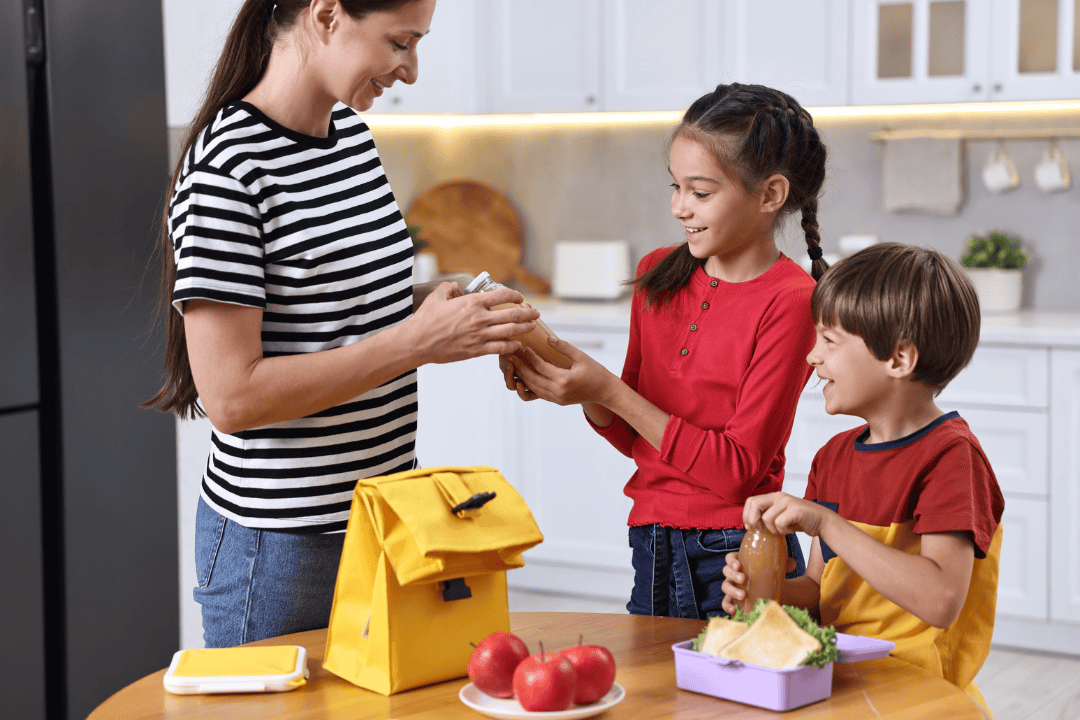 Mother and children preparing healthy school lunches at table in kitchen
