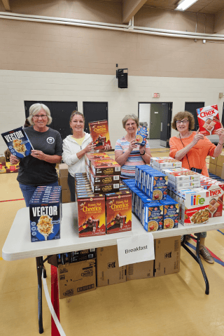 Summer Starfish volunteers holding cereal boxes, standing behind table with rows of cereal boxes