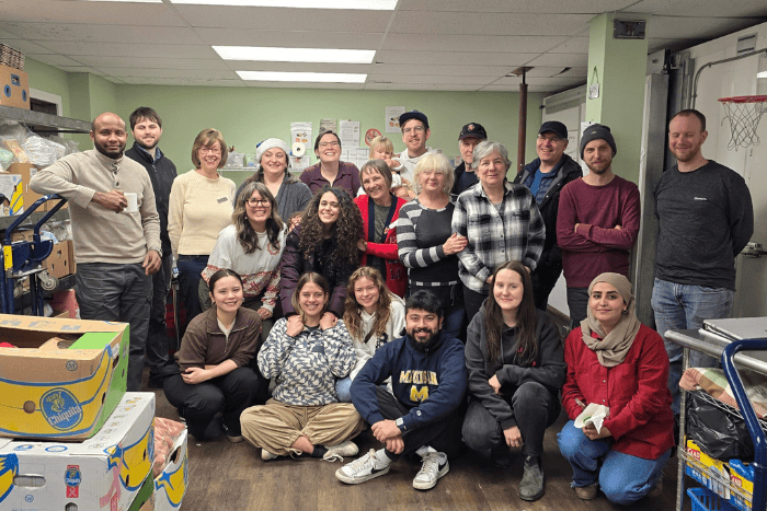 Archway Food Bank team surrounded by boxes of food donations in two rows, top row standing, bottom row sitting, smiling