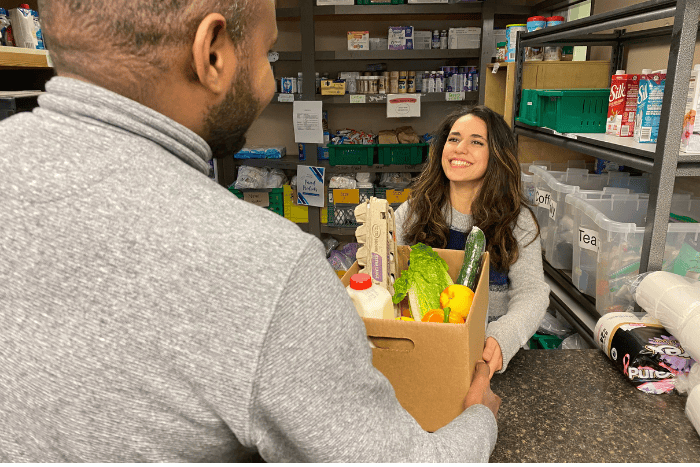 Staff member handing over a hamper of food items A woman handing a box of food to a man