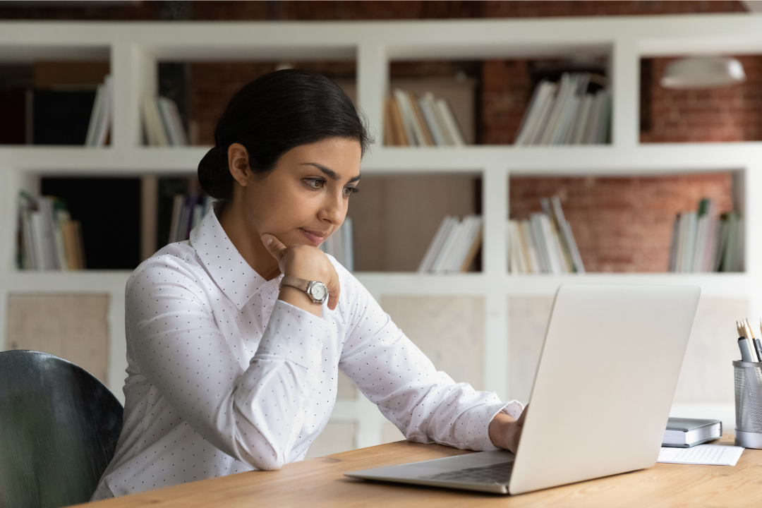 Bahare sitting at a desk on her laptop, wearing a white button up shirt.