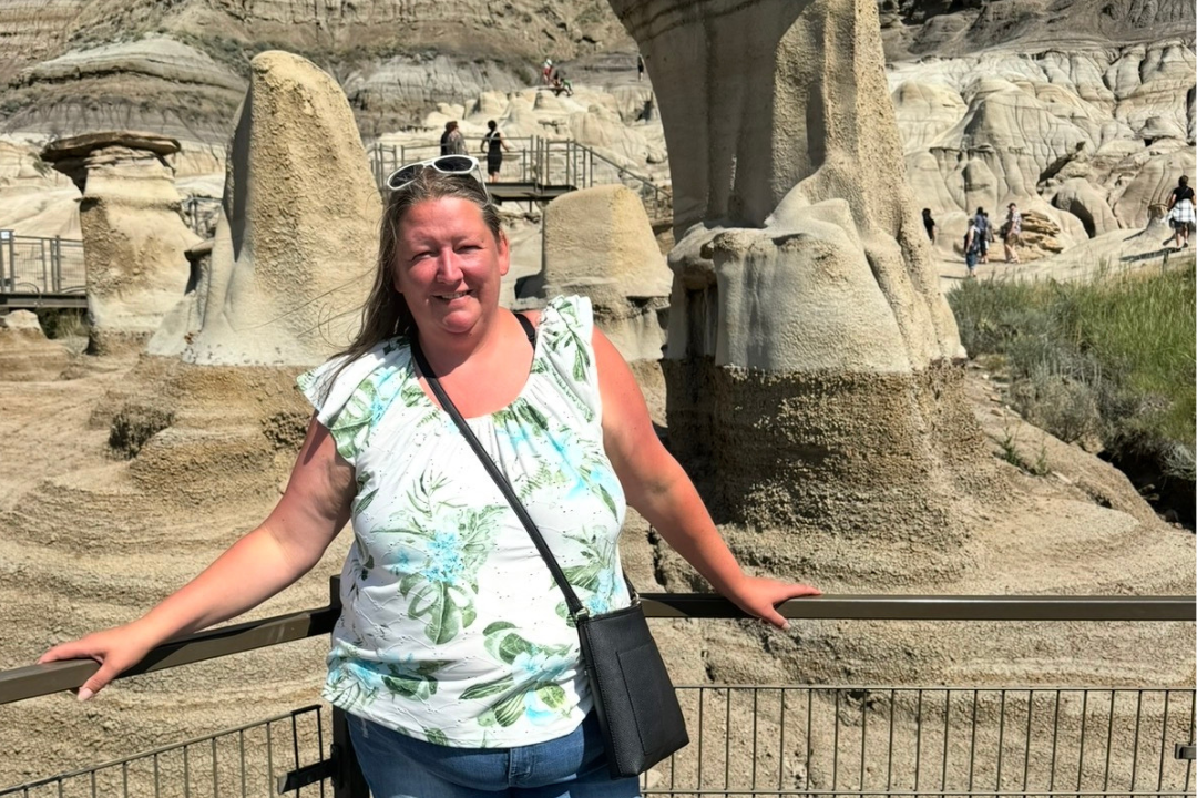 Laura, a middle aged woman with long brown hair, stands in front of various rock formations.