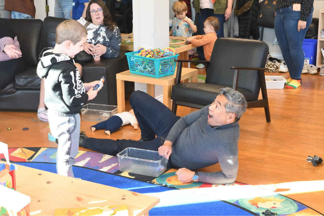 Child showing a toy to an adult who is laying on the ground